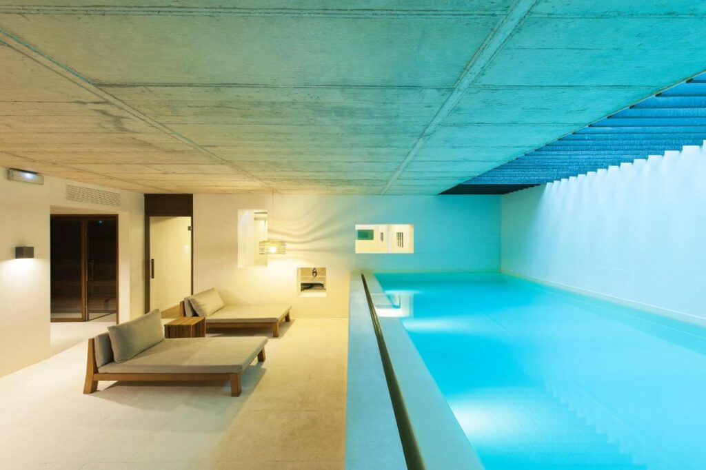 13 Unique Hotels in Barcelona, Spain 5 A modern indoor pool area with turquoise water, minimalist lounge chairs, and concrete ceilings creates a serene, luxurious atmosphere—perfect for those seeking unique hotels in Barcelona.