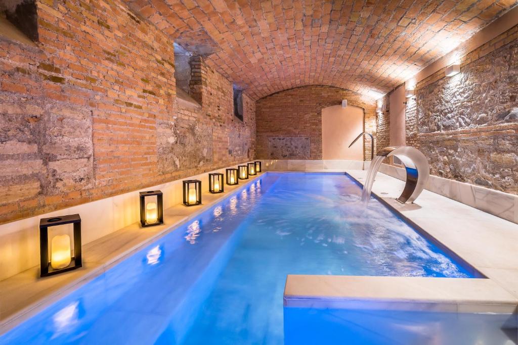 A narrow indoor pool with blue water, surrounded by stone and brick walls, arched brick ceiling, and lit by decorative lanterns along the edge—just like the elegant pools found in boutique hotels in Granada—creates a cozy, relaxing atmosphere.