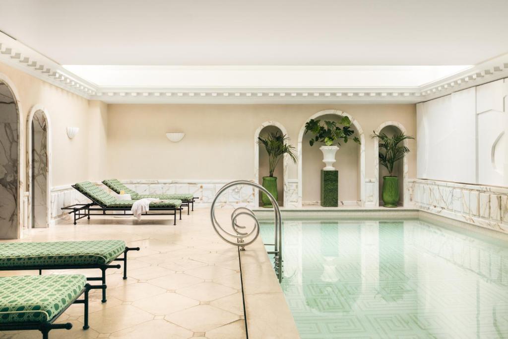 13 Unique Hotels in Paris for a Stylish Stay 35 Indoor swimming pool area with green patterned lounge chairs, marble flooring, arched alcoves with large green vases and plants, and soft lighting—offering the serene, luxurious ambiance found in unique hotels in Paris.