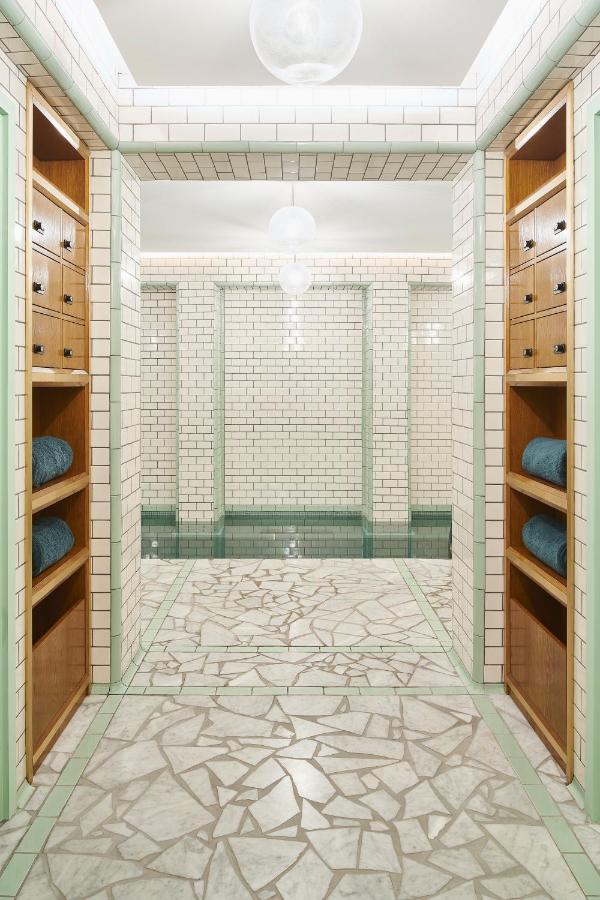 13 Unique Hotels in Paris for a Stylish Stay 20 A bright, tiled locker room in one of the unique hotels in Paris features green and white walls, a mosaic-patterned floor, wooden shelves with folded towels, and spherical ceiling lights overhead.
