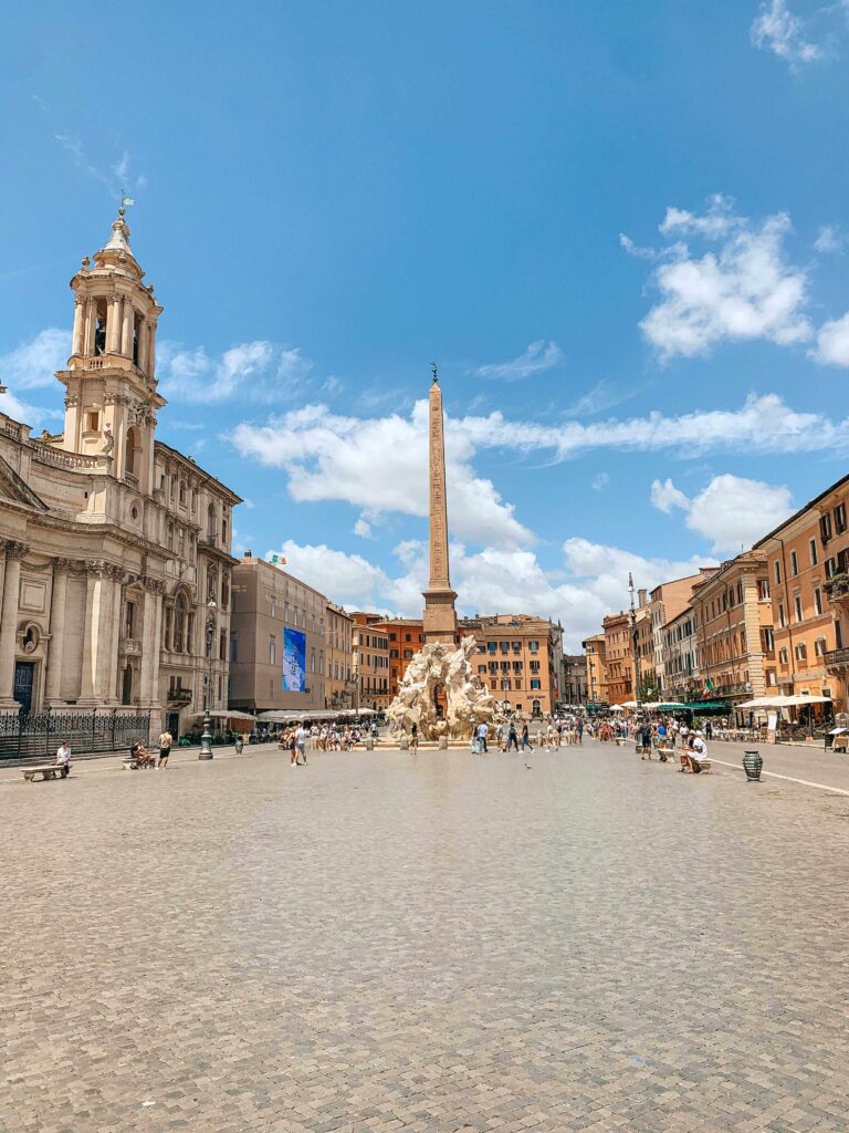 3 Days in Rome Itinerary 11 A sunny day at Piazza Navona in Rome, featuring the Fountain of the Four Rivers and nearby boutique hotels in Rome, all set against historic buildings and a bright blue sky with scattered clouds.