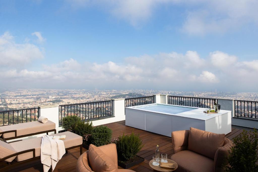 13 Unique Hotels in Barcelona, Spain 48 A rooftop terrace at one of the unique hotels in Barcelona features lounge chairs, potted plants, a table with drinks, and a small pool overlooking the cityscape under a blue sky with scattered clouds.