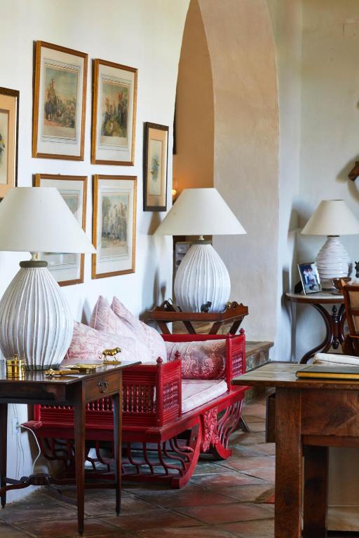 TOP 10 Luxury Hotels in Andalucía 16 A cozy living space reminiscent of luxury hotels in Andalucía, with framed wall art, a red wooden settee with pink cushions, two white ribbed table lamps, a wooden side table, rustic decor, and terracotta tile floors.