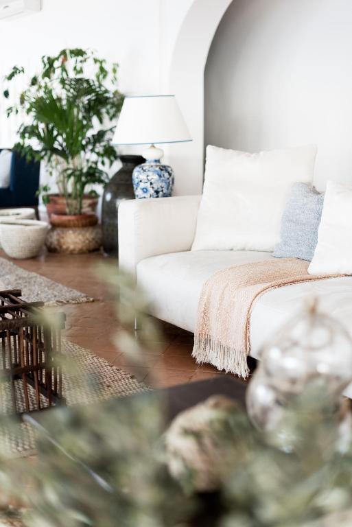 7 Best Hotels in the Aeolian Islands 9 A cozy living room reminiscent of the best hotels in the Aeolian Islands, featuring a white sofa, light blue and cream cushions, a beige throw, potted plants, a blue and white lamp, woven baskets, and a coffee table with stylish decorative items.