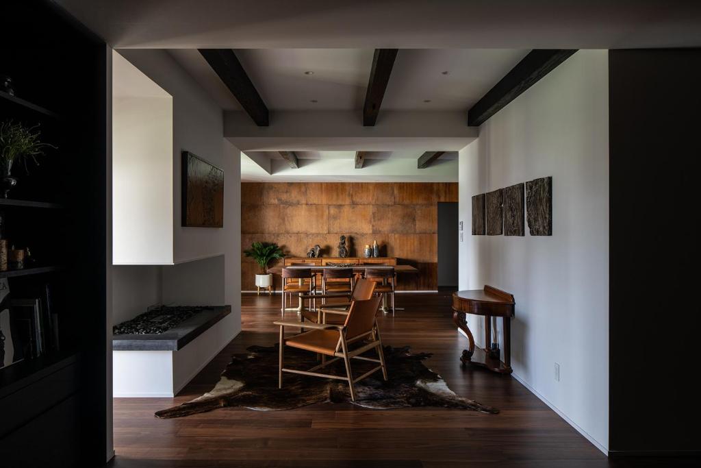 7 Best Hotels in Hiroshima, Japan 25 Modern living and dining area with dark wood floors, white walls, exposed ceiling beams, and minimalist furnishings reminiscent of the best hotels in Hiroshima—wooden chairs, a dining table, cowhide rug, wall art, and a built-in fireplace on the left.