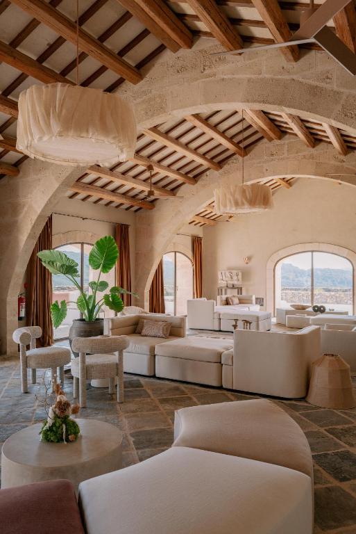 Unique Boutique Hotels in Menorca 44 Spacious living room with arched stone ceilings, beige modern furniture, large windows with mountain views—reminiscent of boutique hotels in Menorca. Indoor plants and pendant lights fill the elegant, airy space with natural light.