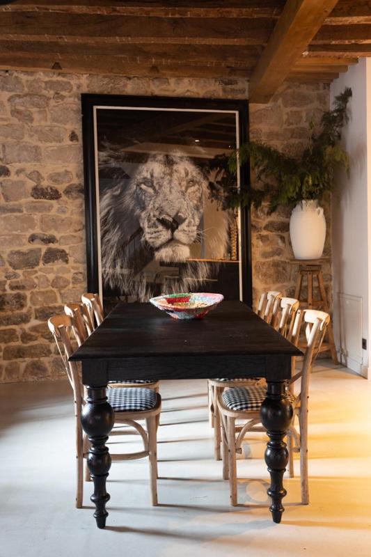 A dining room in the style of fine hotels in Cantabria, featuring a dark wooden table, eight wooden chairs, a black-and-white lion portrait on a stone wall, a potted plant, and a decorative bowl on the table.
