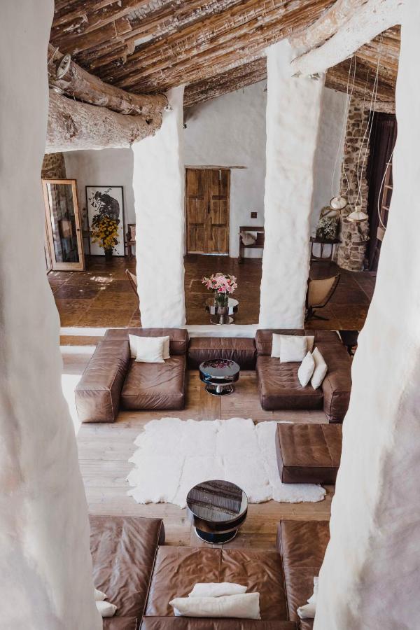 TOP 10 Luxury Hotels in Andalucía 4 Rustic living room with rough white columns, wooden ceiling beams, and brown leather sofas around a white rug—reminiscent of the warm, inviting spaces found in luxury hotels in Andalucia. Natural light enhances its cozy atmosphere.
