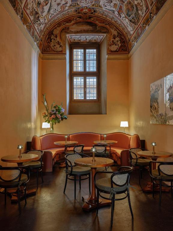 13 UNIQUE Boutique Hotels in Rome 51 Elegant café with round tables, black chairs, and a curved pink sofa under a tall, ornate frescoed ceiling—just the kind of stylish ambiance you'd expect in boutique hotels in Rome. Light pours in from a large window, creating a warm, inviting atmosphere.