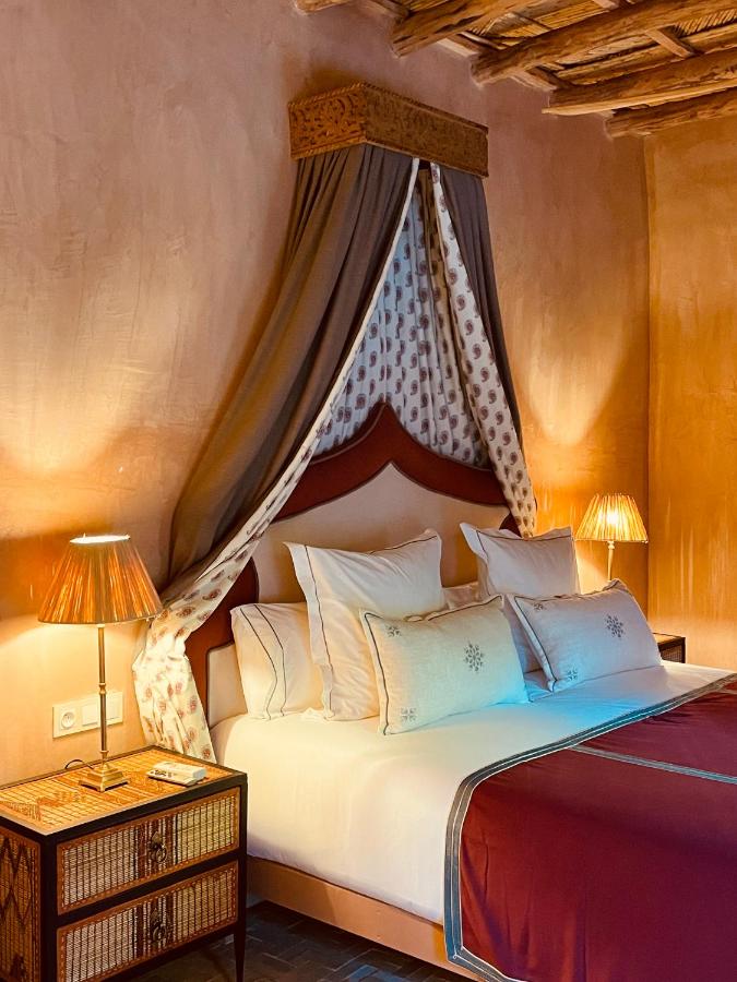 10 Unique Riads in Marrakech with Pool 19 A cozy bedroom inspired by riads in Marrakech with pool, featuring white and beige pillows, an embroidered duvet, and a canopy. Patterned wooden nightstands with warm-lit lamps enhance the rustic, earthy walls and ceiling.