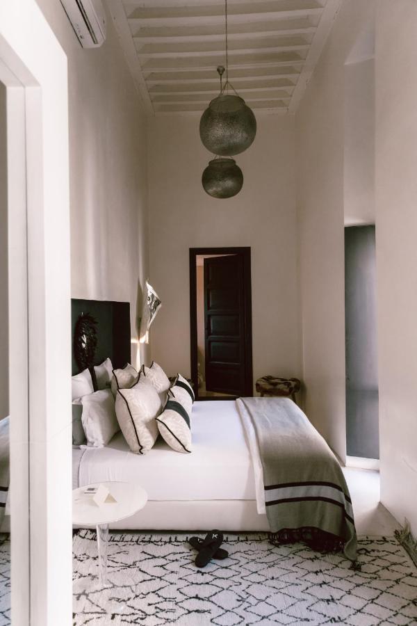 10 Unique Riads in Marrakech with Pool 29 A cozy bedroom inspired by riads in Marrakech with pool, featuring a neatly made bed, white and gray bedding, decorative pillows, pendant lights, a patterned rug, and an open door leading to a dim hallway.