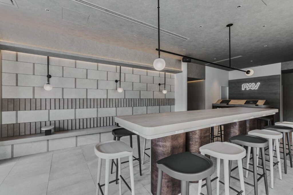 7 Best Hotels in Hiroshima, Japan 9 A modern, minimalist cafe interior found in some of the best hotels in Hiroshima, Japan, featuring a long central table with stools, geometric wall panels, pendant lights, and a glowing FAV sign above the counter.