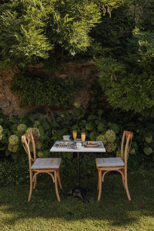 A small outdoor table with two chairs is set on grass, surrounded by lush greenery. Reminiscent of garden dining at charming hotels in Cantabria, the table holds drinks, plates of food, and cups, creating a peaceful scene.