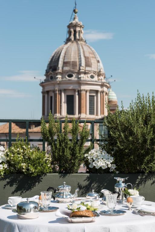 3 Days in Rome Itinerary 5 A table set for breakfast with tea, juice, and pastries on a terrace at one of the boutique hotels in Rome, with lush plants and a large domed building in the background under a clear blue sky.