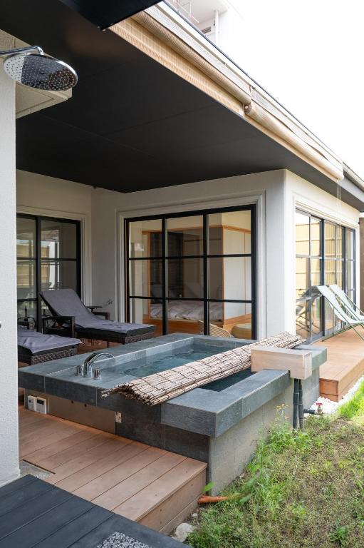 7 Best Hotels in Hiroshima, Japan 22 Modern outdoor patio with a small rectangular stone hot tub, lounge chairs, and large sliding glass doors leading to an indoor living space—reminiscent of the best hotels in Hiroshima. A bamboo mat covers part of the tub, surrounded by green grass.