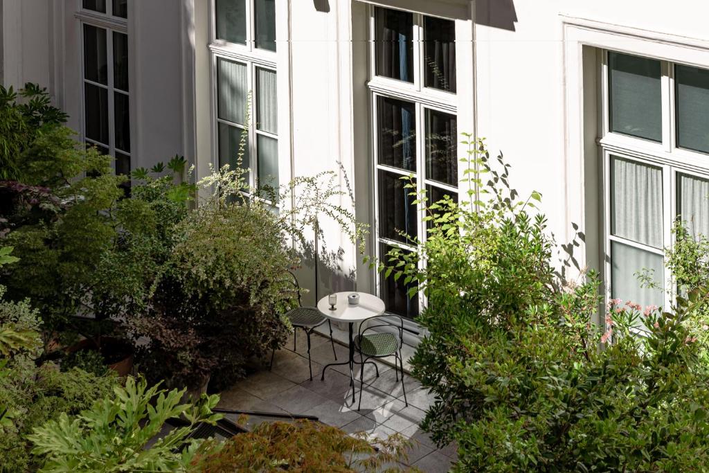 13 Unique Hotels in Paris for a Stylish Stay 56 A small patio with two green chairs and a round white table sits among lush green plants outside tall windows of a white building, creating a peaceful outdoor setting reminiscent of unique hotels in Paris.