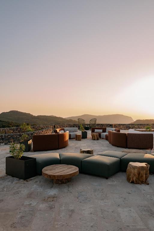 Unique Boutique Hotels in Menorca 43 A modern outdoor lounge area with low cushioned seating and wooden tables sits on a stone patio at sunset, overlooking distant hills—a serene setting reminiscent of boutique hotels in Menorca under a clear sky.