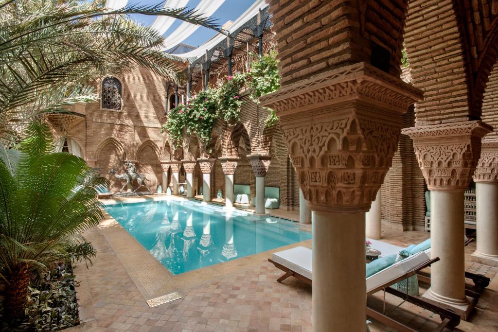 10 Unique Riads in Marrakech with Pool 40 A luxurious courtyard pool, typical of riads in Marrakech with pool, is framed by ornate columns, lush greenery, and traditional Moroccan architecture. Sun loungers and shade sails complete the relaxing atmosphere.