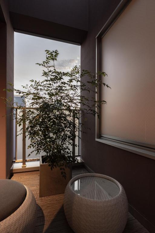 7 Best Hotels in Hiroshima, Japan 27 A small, modern balcony at one of the best hotels in Hiroshima features a tall potted plant, a round white wicker table, and a cushioned seat. Soft daylight filters through frosted glass and the railing, creating a peaceful ambiance.