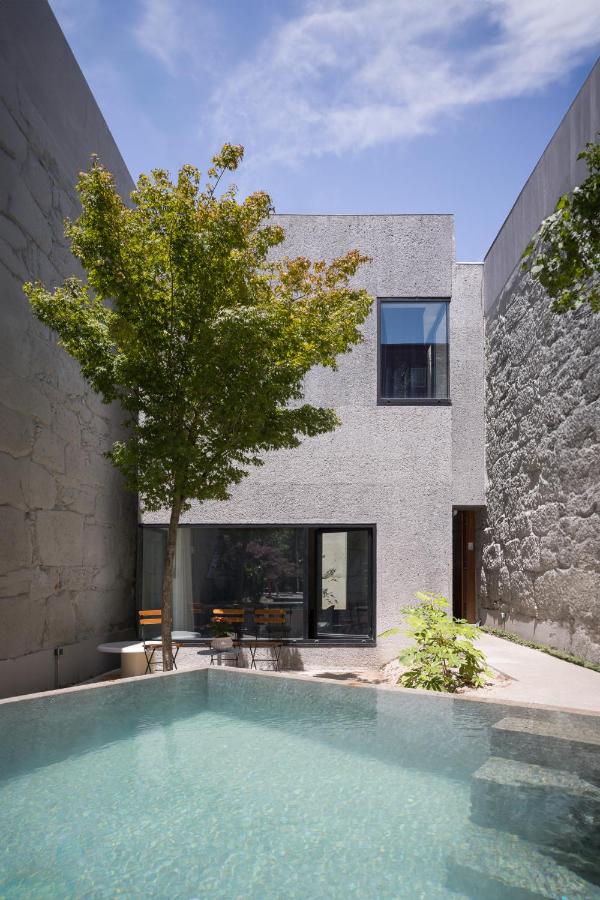 Top 12 Boutique Hotels in Porto, Portugal 16 A modern, minimalist gray house with large windows sits next to a small pool and a tree, surrounded by high stone walls under a partly cloudy sky—reminiscent of the unique charm found at boutique hotels in Porto.
