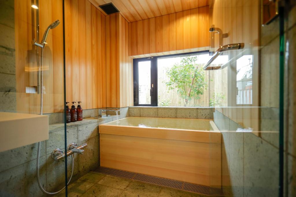 15 Unique Hotels in Tokyo: Coolest hotels 43 Modern bathroom in the style of unique hotels in Tokyo, featuring wood-paneled walls and ceiling, gray stone accents, a deep wooden soaking tub by a garden-view window, and a sleek glass-enclosed shower with mounted toiletries.
