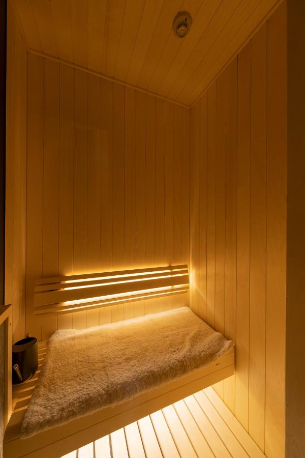 15 Unique Hotels in Tokyo: Coolest hotels 36 A small wooden sauna with light-colored paneling, a bench covered with a towel or mat, and soft lighting beneath the bench—just one serene feature you might find at unique hotels in Tokyo. A sauna bucket and ladle sit quietly in the corner.