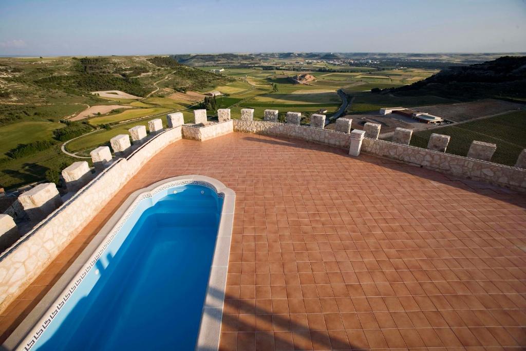 4 Best Hotels in Ribera del Duero, Spain 24 A small, rectangular swimming pool sits on a spacious tiled terrace with stone walls, much like the charming pools at hotels in Ribera del Duero, overlooking expansive green fields and rolling hills under a clear sky.