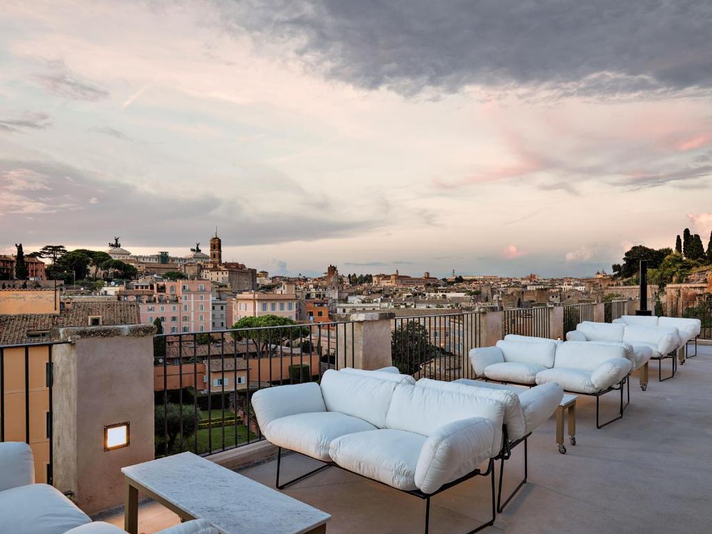13 UNIQUE Boutique Hotels in Rome 33 Rooftop terrace with white cushioned lounge chairs and tables, overlooking a cityscape with historic buildings under a cloudy evening sky—an inviting scene found at boutique hotels in Rome.