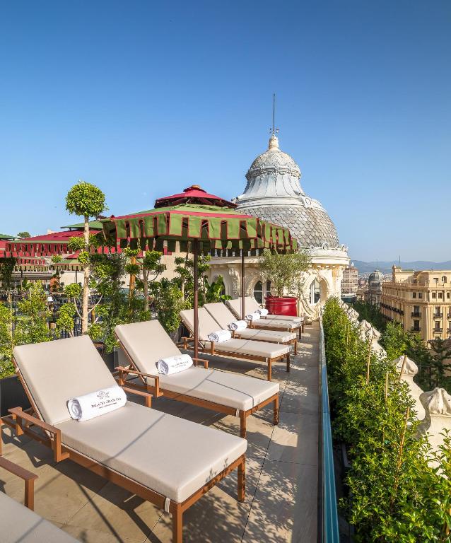 Rooftop terrace at one of the boutique hotels in Granada, featuring sun loungers, rolled towels, potted plants, and green-striped umbrellas overlooking elegant historic buildings under a clear blue sky.