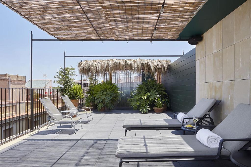 13 Unique Hotels in Barcelona, Spain 33 A sunny rooftop terrace at one of the unique hotels in Barcelona, featuring lounge chairs, rolled white towels, green plants, and a bamboo-shaded pergola. The space is bordered by a black metal railing and beige tiled walls.