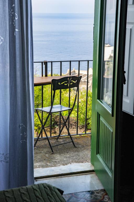 7 Best Hotels in the Aeolian Islands 26 A metal chair sits on a small balcony overlooking the ocean, seen through a partially open green door and sheer curtain. Sunlight bathes the scene, evoking tranquil mornings at hotels in the Aeolian Islands, with greenery visible beyond the railing.