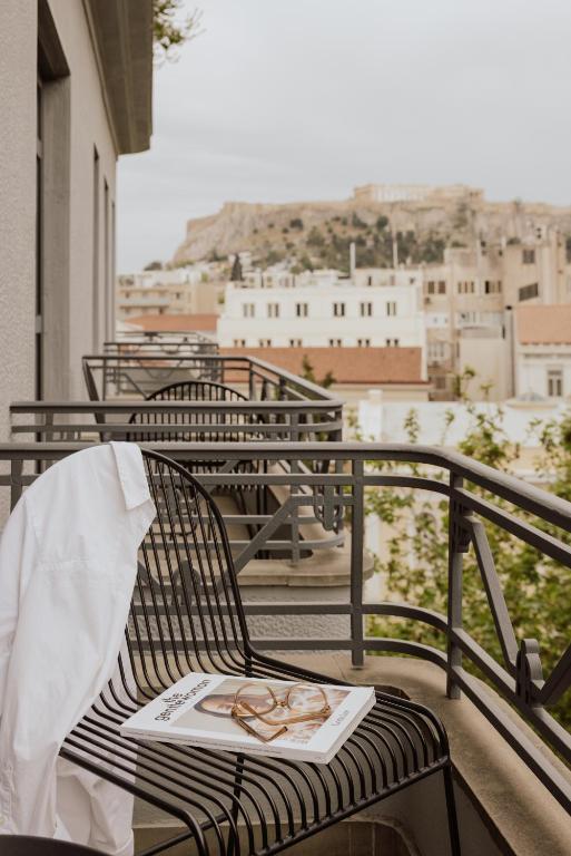 A white shirt and glasses rest on a black chair on a balcony overlooking a city with the Acropolis in the distance—an inviting scene often found at boutique hotels in Athens.