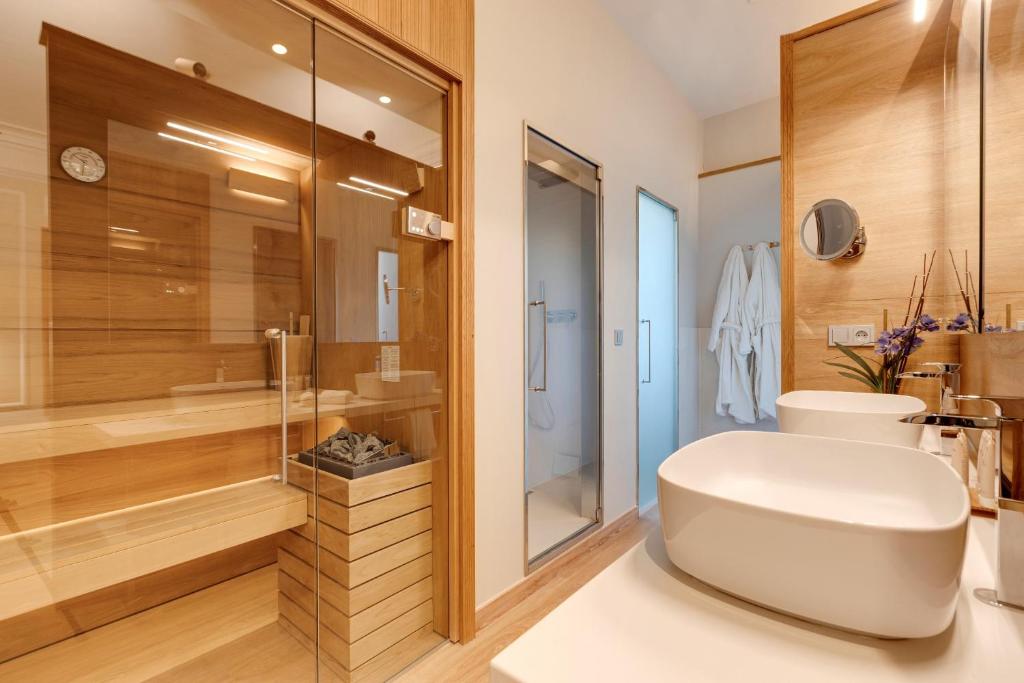 13 Unique Hotels in Barcelona, Spain 36 Modern bathroom with light wood accents, a glass-enclosed sauna, dual white vessel sinks, a wall mirror, shower area, and two white bathrobes—perfect for those seeking unique hotels in Barcelona.