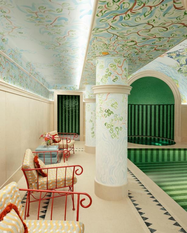 13 Unique Hotels in Paris for a Stylish Stay 38 A luxurious indoor pool with green striped tiles, ornate painted columns, patterned ceiling, and walls evokes the charm of unique hotels in Paris. Patio chairs with yellow cushions and a table with flowers enhance the vibrant, elegant atmosphere.
