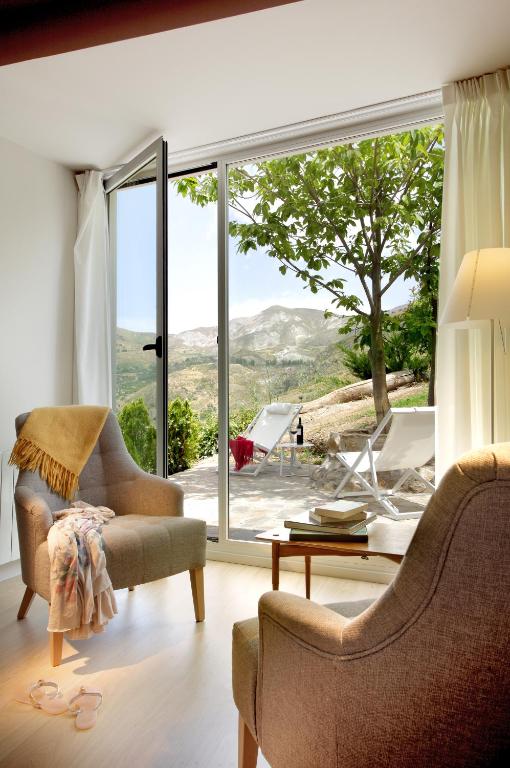 TOP 10 Luxury Hotels in Andalucía 28 Modern sitting area with two armchairs near a glass door, opening to a patio with lounge chairs and mountain views; reminiscent of the serene indoor-outdoor spaces found in luxury hotels in Andalucía, with sunlight streaming in for a cozy ambiance.