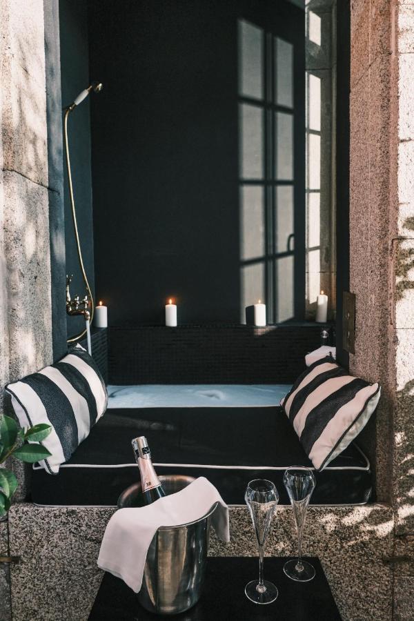 Top 12 Boutique Hotels in Porto, Portugal 9 A cozy, black and white nook with striped pillows, lit candles, and a built-in tub—just like the intimate corners found in boutique hotels in Porto. In the foreground, a table holds a champagne bottle on ice and two empty glasses. Sunlight streams in through a window.