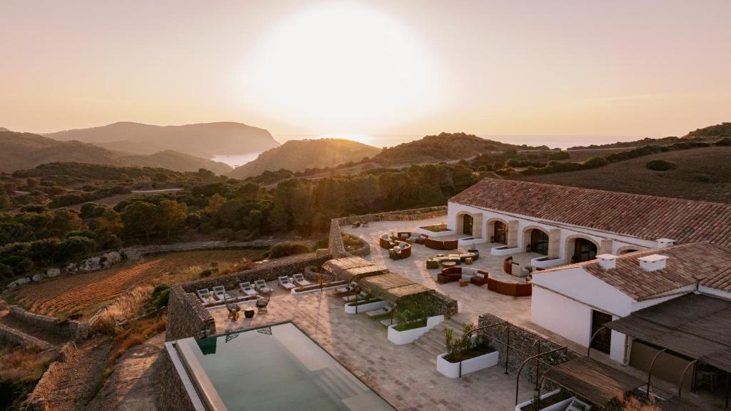 Unique Boutique Hotels in Menorca 1 Vestige Son Ermita Hotel with a pool and outdoor seating overlooks rolling hills and a distant bay at sunset, surrounded by natural landscape and mountains—echoing the charm of boutique hotels in Menorca.