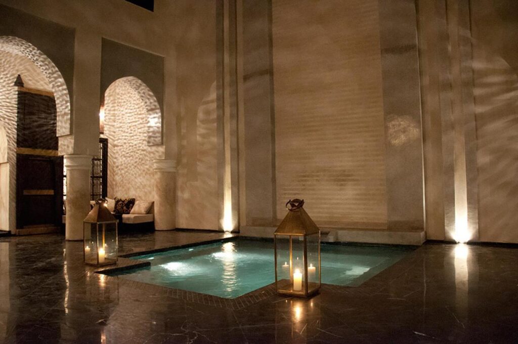 10 Unique Riads in Marrakech with Pool 2 A small indoor pool is softly lit by lanterns and candles, casting intricate shadows on the walls. Reminiscent of riads in Marrakech with pool, the space features arches, marble floors, and a cozy seating area for a tranquil ambiance.