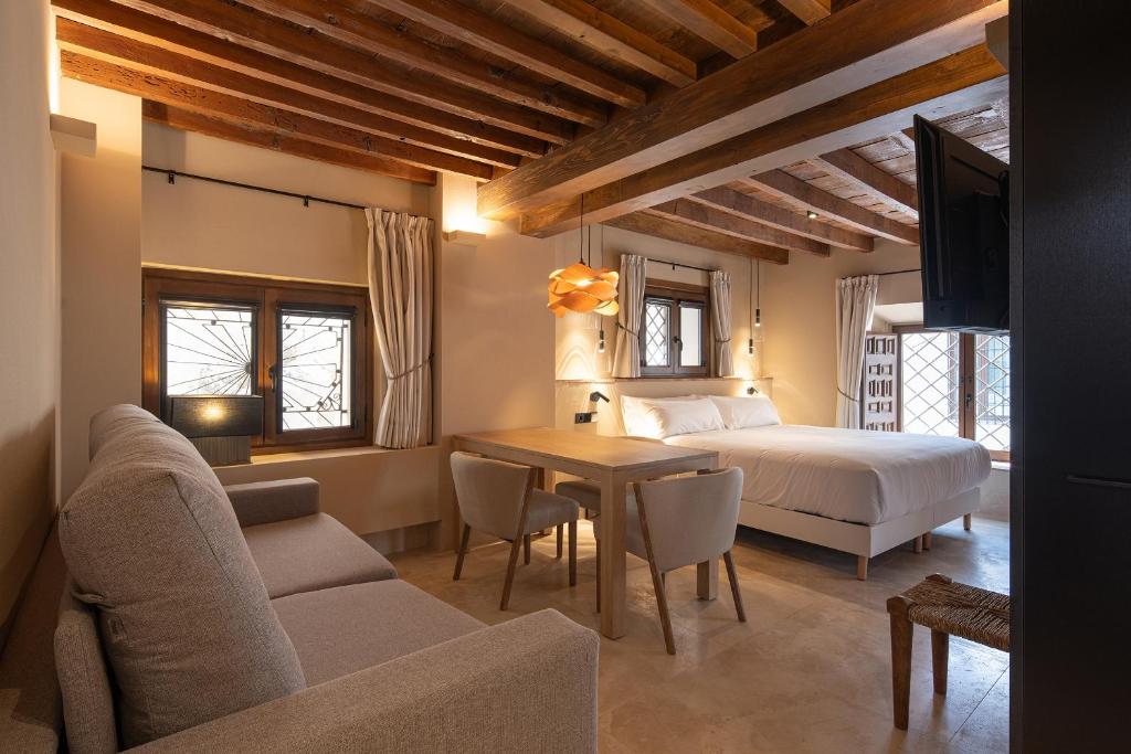 A cozy hotel room with wooden ceiling beams, a large bed, a sofa, and dining table welcomes you with natural light and warm ambiance—perfect for those seeking boutique hotels in Granada.