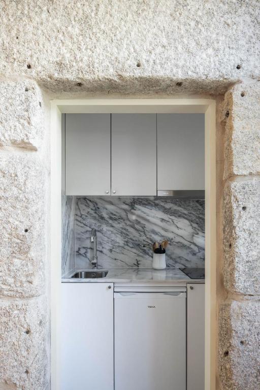 Top 12 Boutique Hotels in Porto, Portugal 42 A small modern kitchen with white cabinets, marble backsplash and countertop, a compact sink, and utensils in a white holder—echoing the chic style often found in boutique hotels in Porto—framed by a textured stone doorway.