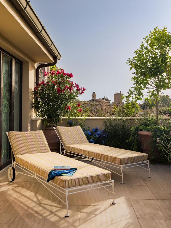 3 Days in Rome Itinerary 4 Two striped lounge chairs with a blue towel rest on a sunny terrace filled with potted plants and flowers, overlooking a cityscape of historic buildings—capturing the elegant charm found at boutique hotels in Rome under a clear blue sky.