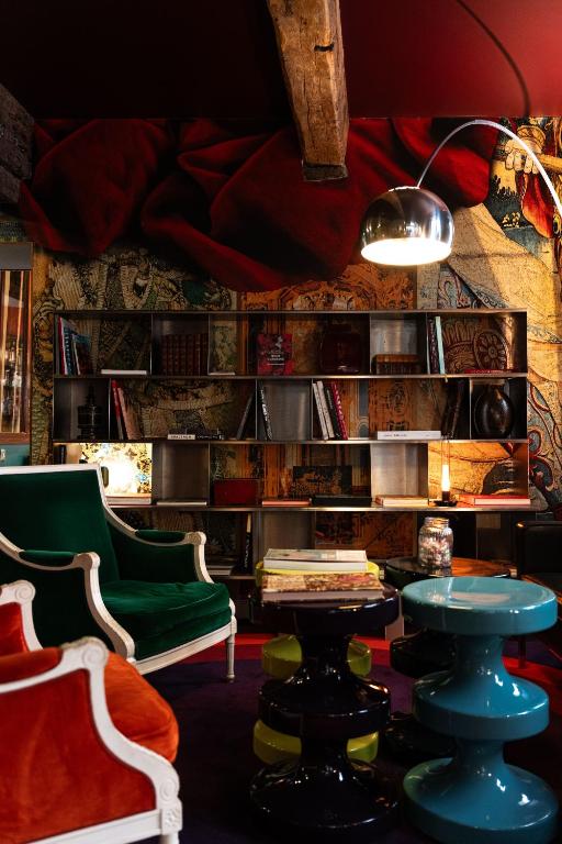 13 Unique Hotels in Paris for a Stylish Stay 49 A cozy, eclectic library in one of the most unique hotels in Paris, with velvet green and orange armchairs, colorful tables, a metal floor lamp, a wall of bookshelves, tapestry artwork, all under wooden ceiling beams and warm lighting.
