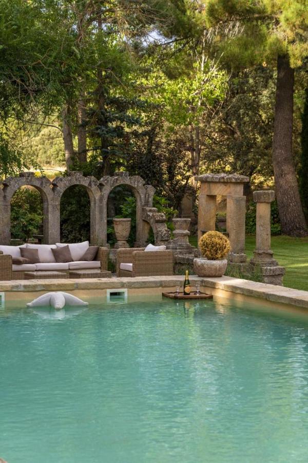 Unique Hotels in Soria: Northern Castile 2 Luxurious outdoor pool with turquoise water at one of the top hotels in Soria, surrounded by wicker lounge furniture and stone archways. A tray with wine floats on the pool, while lush trees and grass create a relaxing garden setting.