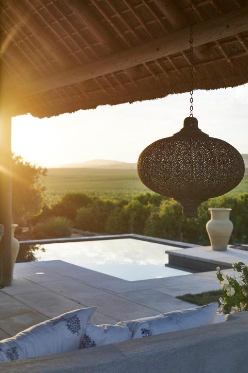 TOP 10 Luxury Hotels in Andalucía 15 A decorative hanging lantern under a patio roof overlooks a serene pool and open landscape at sunset, evoking the tranquil elegance often found in luxury hotels in Andalucía, with pillows on a sofa and large vases in the background.