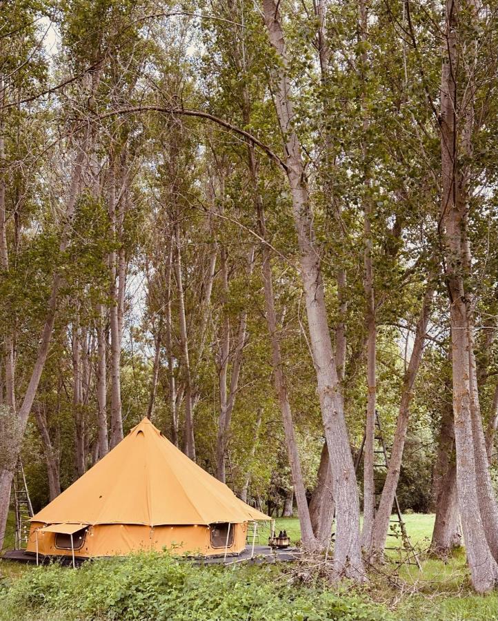 A large yellow tent is set up on a wooden platform among tall, leafy trees in a green forest clearing, offering a unique glamping experience reminiscent of the nature retreats found at hotels in Cantabria.