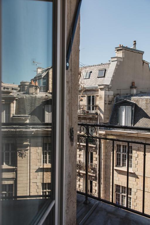13 Unique Hotels in Paris for a Stylish Stay 31 View from a balcony with a metal railing, overlooking classic Parisian-style buildings with sloped roofs and chimneys under a clear blue sky. A window frame is visible in the foreground—typical of unique hotels in Paris.