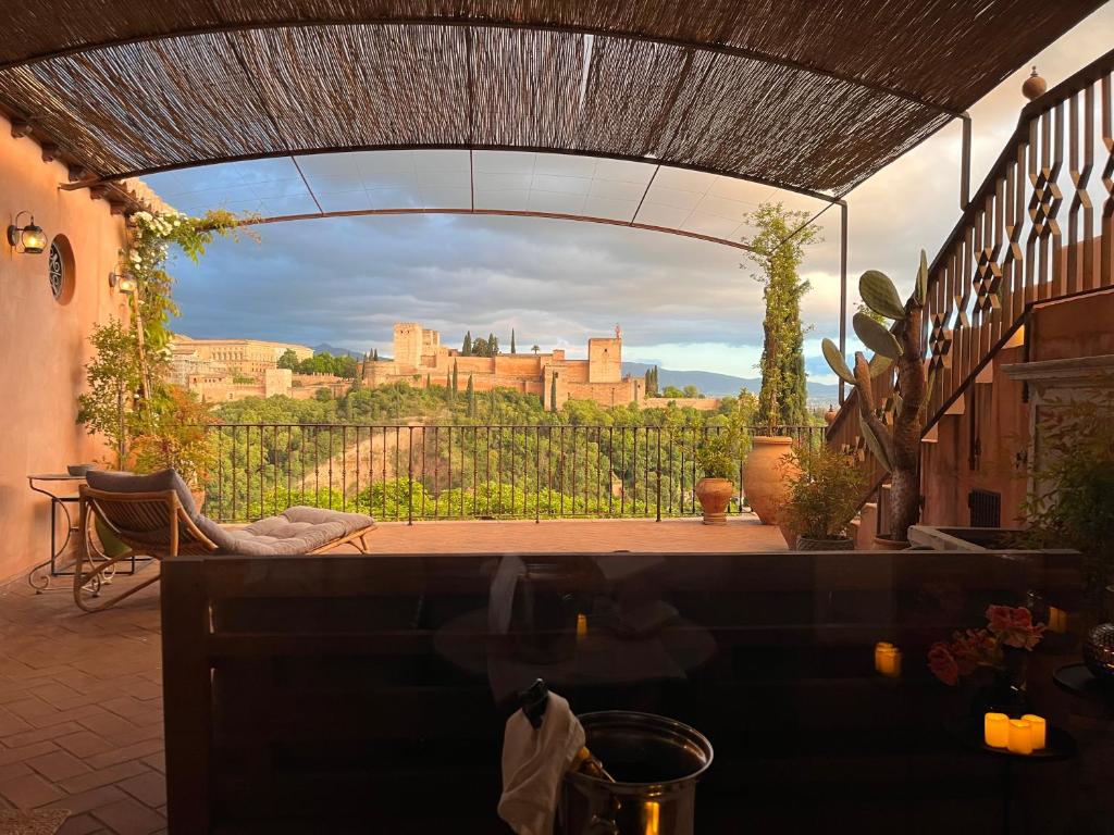 A cozy terrace with a lounge chair and potted plants overlooks a scenic view of the Alhambra palace, much like the charming outdoor spaces found at boutique hotels in Granada, all bathed in warm evening light under a rustic pergola.