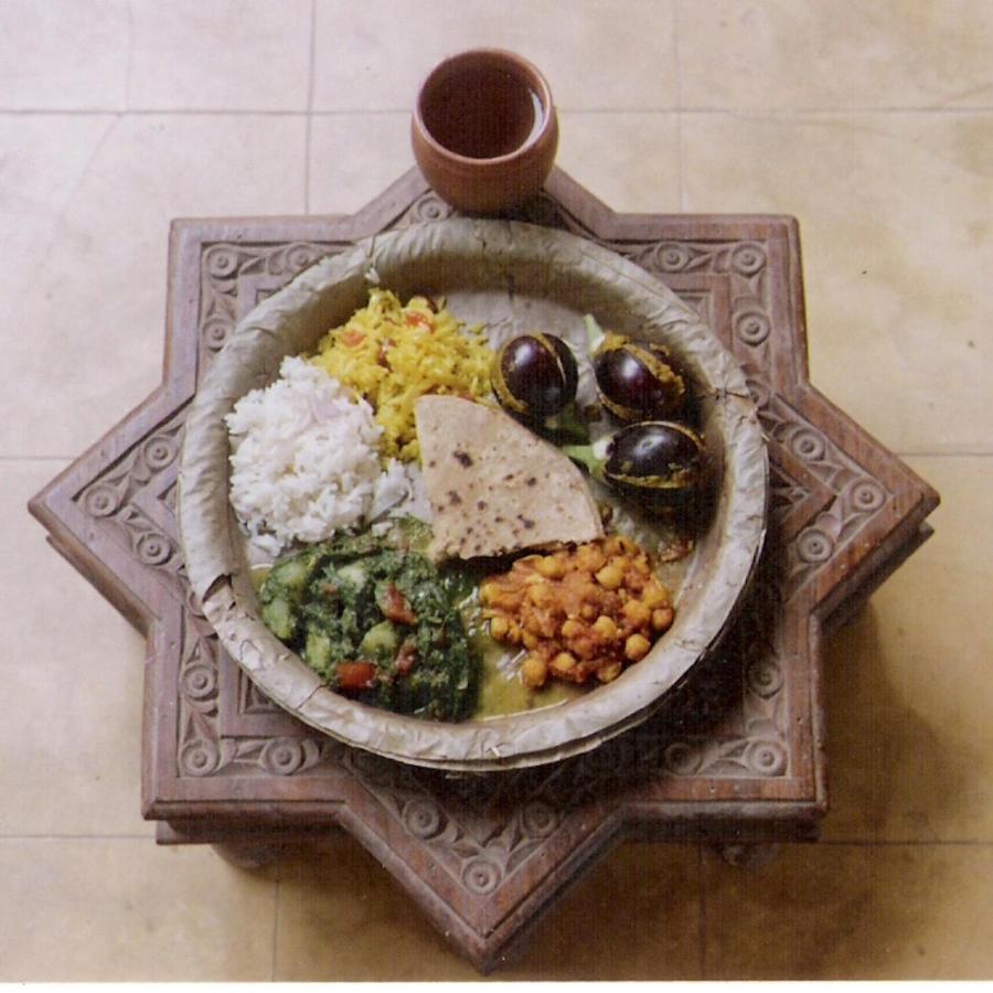 Authentic Heritage Hotels in Mandawa 8 A leaf plate holds rice, yellow pilaf, chapati, spiced chickpeas, cooked greens, three boiled eggs, and a clay cup, all set on a carved star-shaped wooden stand—an authentic taste often enjoyed at hotels in Mandawa.