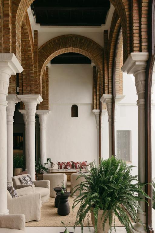 TOP 10 Luxury Hotels in Andalucía 25 A stylish indoor lounge, inspired by luxury hotels in Andalucía, features cream sofas, patterned cushions, potted green plants, and tall brick arches supported by white columns for a warm and inviting atmosphere.
