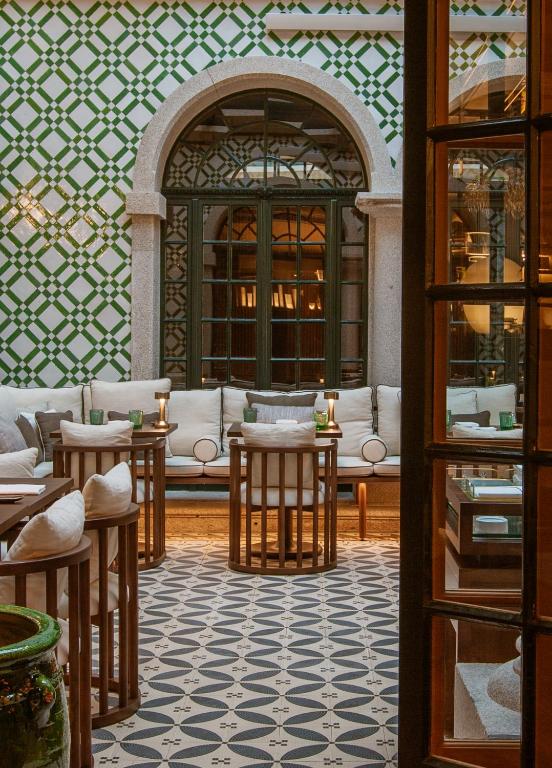 Top 12 Boutique Hotels in Porto, Portugal 49 Elegant indoor patio reminiscent of boutique hotels in Porto, with patterned tile floor, cushioned bench seating, small round wooden tables, and arched windows. Green and white geometric tiles add a stylish, inviting atmosphere.